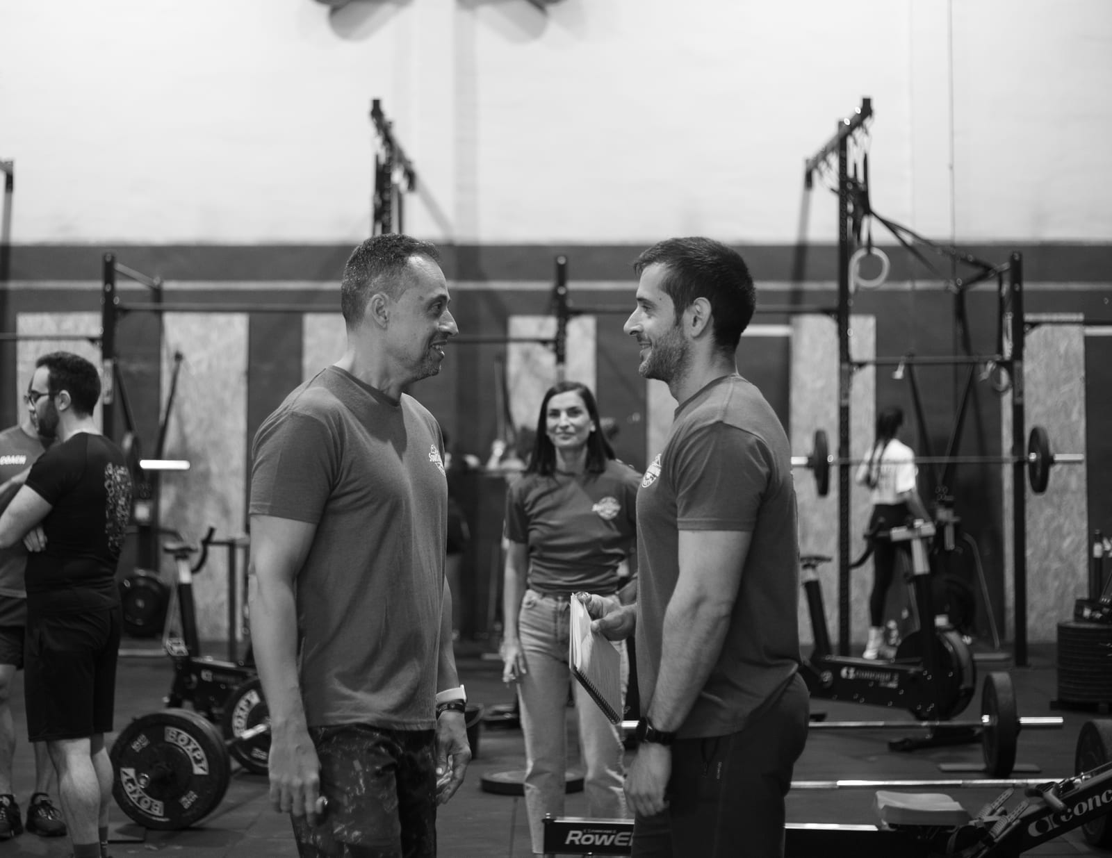 Dos socios charlando entre series, con la sala entrenando alrededor